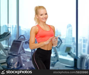 sport, fitness, technology and people concept - smiling sporty woman with smartphone over gym machines background