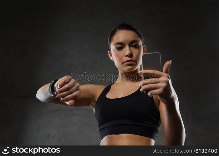 sport, fitness, technology and people concept - young woman with heart-rate watch and smartphone in gym