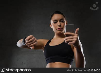 sport, fitness, technology and people concept - young woman with heart-rate watch and smartphone in gym