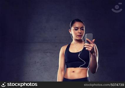 sport, fitness, technology and people concept - young woman with smartphone and earphones listening to music in gym. woman with smartphone and earphones in gym