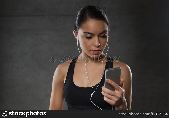 sport, fitness, technology and people concept - young woman with smartphone and earphones listening to music in gym