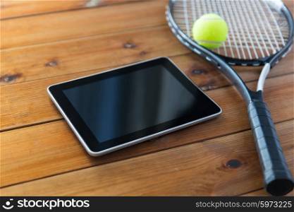 sport, fitness, technology, game and objects concept - close up of tennis racket with ball and tablet pc computer on wooden floor