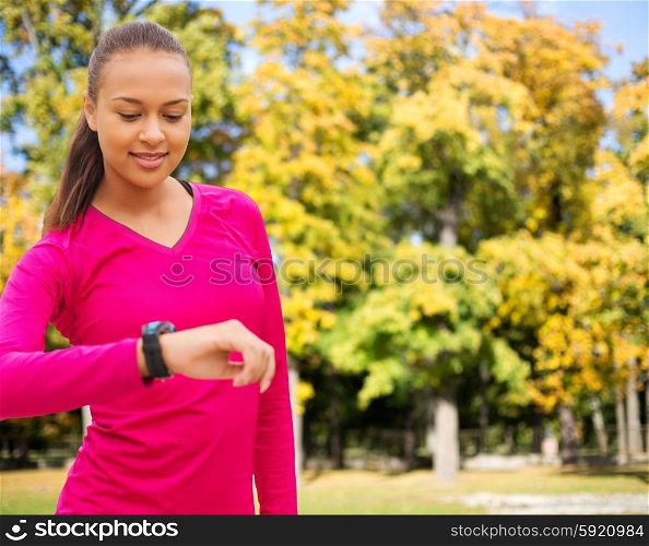 sport, fitness, technology, healthcare and people concept - smiling young african american woman with heart rate watch over autumn park background