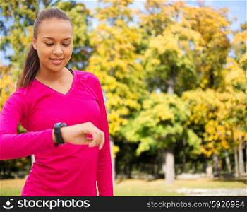 sport, fitness, technology, healthcare and people concept - smiling young african american woman with heart rate watch over autumn park background