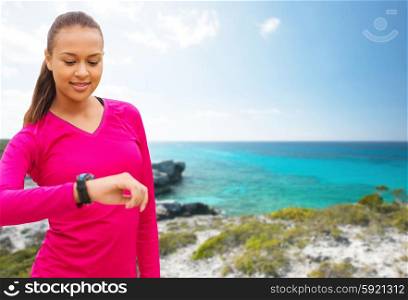 sport, fitness, technology, healthcare and people concept - smiling young african american woman with heart rate watch over beach background