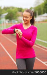 sport, fitness, technology, healthcare and people concept - smiling young woman with heart rate watch on track outdoors