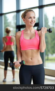 sport, fitness, training, weightlifting and people concept - young sporty woman with dumbbells flexing biceps in gym