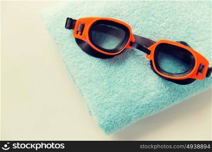 sport, fitness, water sports and objects concept - close up of swimming goggles and towel. close up of swimming goggles and towel
