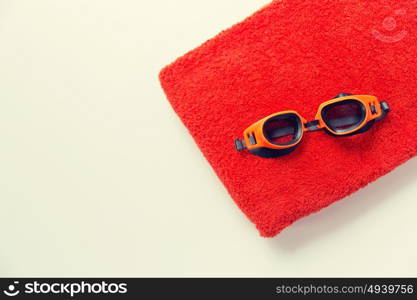 sport, fitness, water sports and objects concept - close up of swimming goggles and towel. close up of swimming goggles and towel