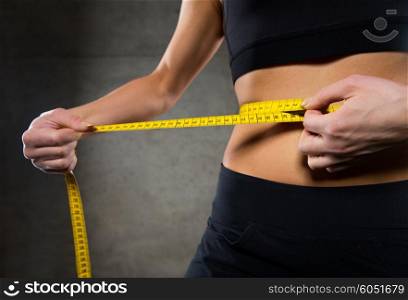 sport, fitness, weight loss, diet and people concept - close up of woman measuring waist size by tape in gym