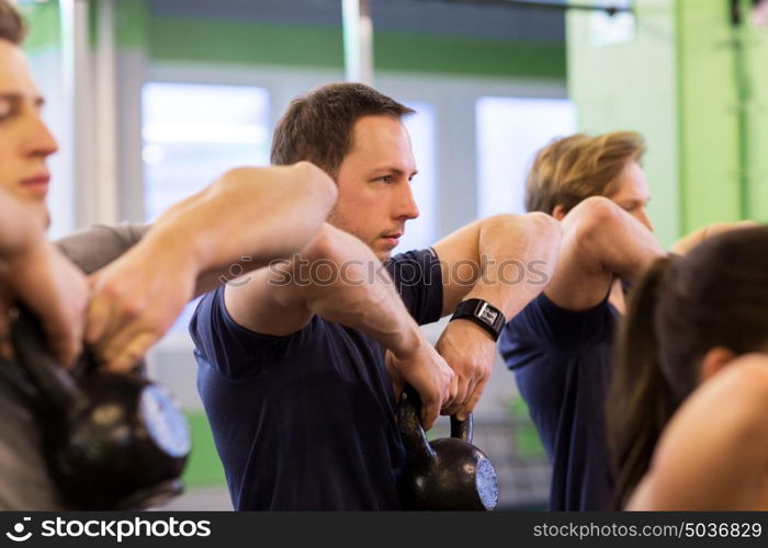 sport, fitness, weightlifting and people concept - man with kettlebell and heart-rate tracker at group training exercising in gym. group of people with kettlebells exercising in gym