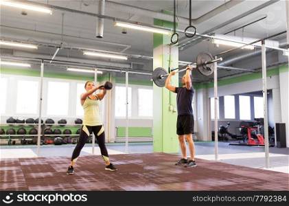 sport, fitness, weightlifting, lifestyle and people concept - man and woman with kettlebell and barbell exercising in gym. man and woman with weights exercising in gym