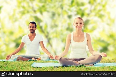 sport, fitness, yoga and people concept - smiling couple meditating and sitting on mats over green tree leaves background