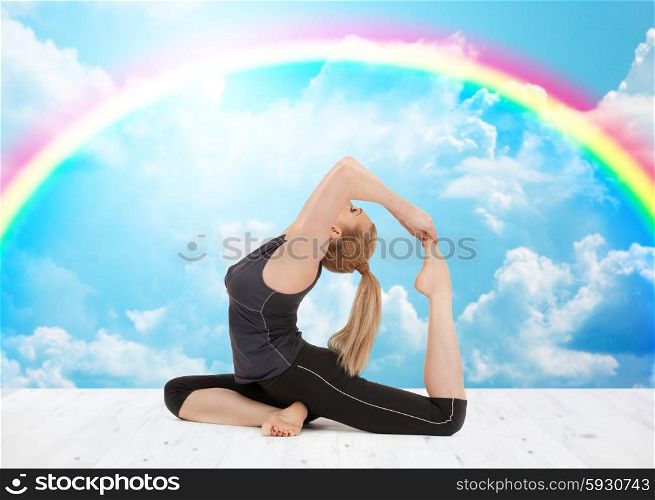 sport, fitness, yoga, people and health concept - happy young woman doing headstand exercise on wooden berth over white clouds and rainbow on blue sky background