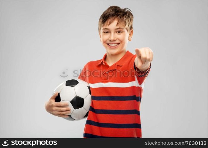 sport, football and leisure games concept - happy smiling boy holding soccer ball and pointing to camera over grey background. happy boy with soccer ball pointing to camera