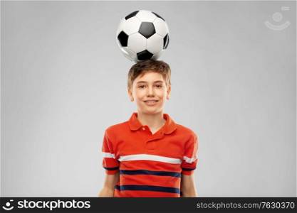 sport, football and leisure games concept - happy smiling boy with soccer ball on his head over grey background. happy smiling boy with soccer ball on his head