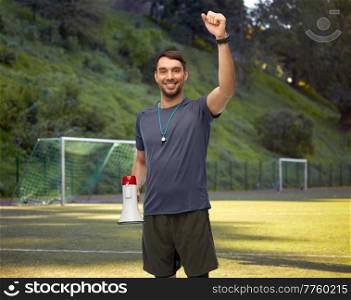 sport, football and people concept - happy smiling male coach or referee with whistle and megaphone celebrating success over soccer field background. happy soccer coach with megaphone on playground