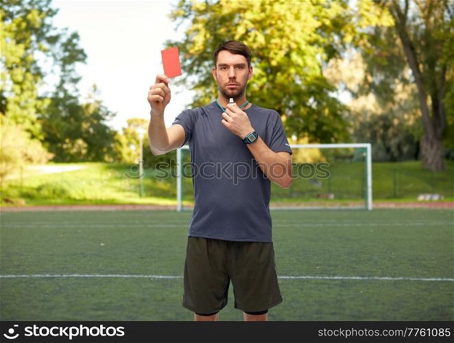 sport, football and refereeing concept - male referee whistling whistle and showing red penalty card over soccer field background. soccer referee with whistle showing red card