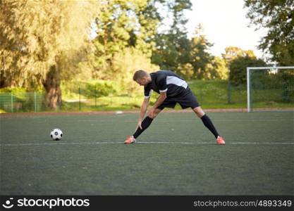 sport, football training and people - soccer player stretching leg on field