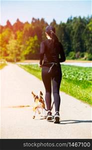 Sport girl is running with a dog (Beagle) on a leash in the spring time, sunny day on the rural road to forest. Copy space in nature. Sport girl is running with a dog (Beagle) on the rural road.