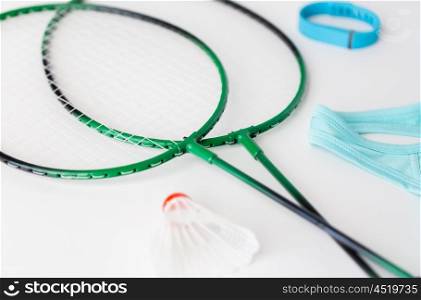 sport, healthy lifestyle and objects concept - close up of badminton rackets with shuttlecock and fitness tracker