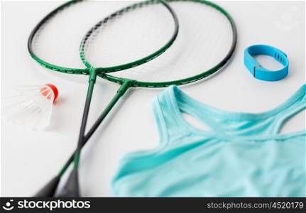sport, healthy lifestyle and objects concept - close up of badminton rackets with shuttlecock, fitness tracker and sports top