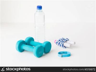 sport, healthy lifestyle and objects concept - close up of dumbbells, fitness tracker, skipping rope and water bottle with water over white background