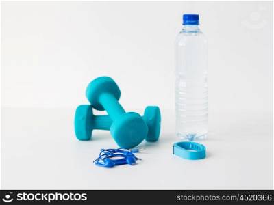 sport, healthy lifestyle and objects concept - close up of dumbbells, fitness tracker, earphones and water bottle over white background