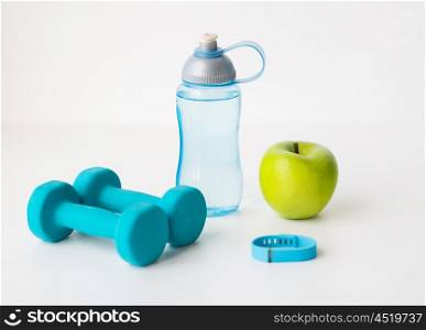 sport, healthy lifestyle and objects concept - close up of dumbbells with fitness tracker, green apple and water bottle over white background