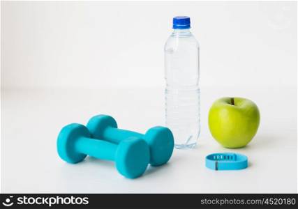 sport, healthy lifestyle and objects concept - close up of dumbbells with fitness tracker, green apple and water bottle over white background