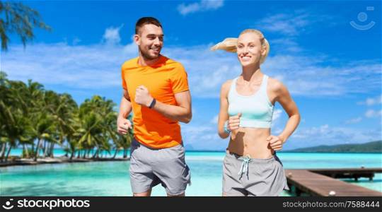 sport, healthy lifestyle and people concept - smiling couple with fitness trackers running at summer over city street on background. smiling couple running along exotic on beach