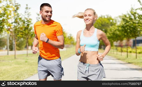 sport, healthy lifestyle and people concept - smiling couple with fitness trackers running along road on city street background. happy couple with fitness trackers running outdoor