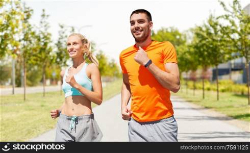 sport, healthy lifestyle and people concept - smiling couple with fitness trackers running along road on city street background. happy couple with fitness trackers running outdoor