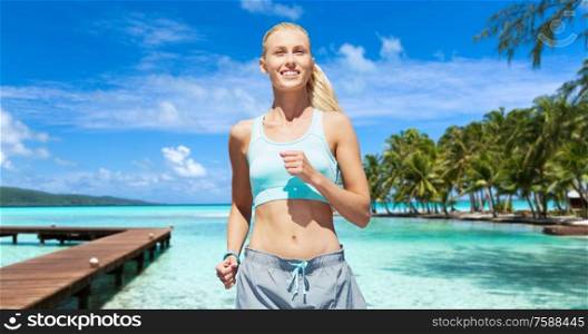 sport, healthy lifestyle and people concept - smiling young woman with fitness tracker running over city street on background. smiling young woman running along exotic beach