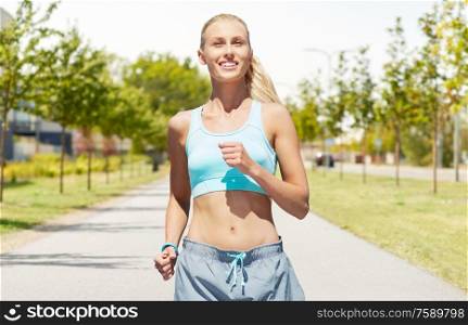 sport, healthy lifestyle and people concept - smiling young woman with fitness tracker running along road on city street background. smiling young woman running outdoors