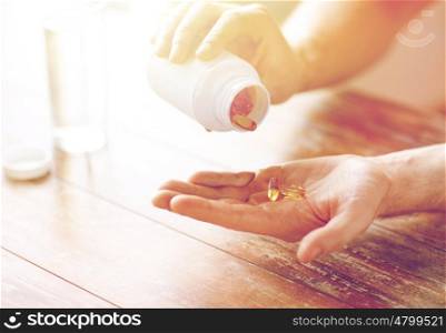 sport, healthy lifestyle, medicine, nutritional supplements and people concept - close up of man in fitness bracelet with glass of water pouring fish oil capsules from jar to hand