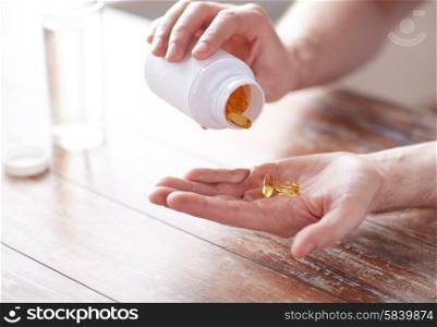 sport, healthy lifestyle, medicine, nutritional supplements and people concept - close up of man in fitness bracelet with glass of water pouring fish oil capsules from jar to hand