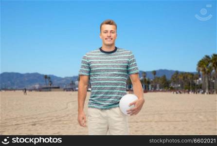 sport, leisure and people concept - smiling young man with volleyball over venice beach background in california. smiling young man with volleyball