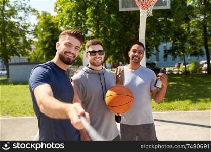 sport, leisure games and male friendship concept - group of happy men or friends taking picture by selfie stick on outdoor basketball playground. happy men taking selfie on basketball playground