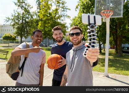 sport, leisure games and male friendship concept - group of happy men or friends taking selfie by smartphone on tripod on outdoor basketball playground. happy men taking selfie on basketball playground