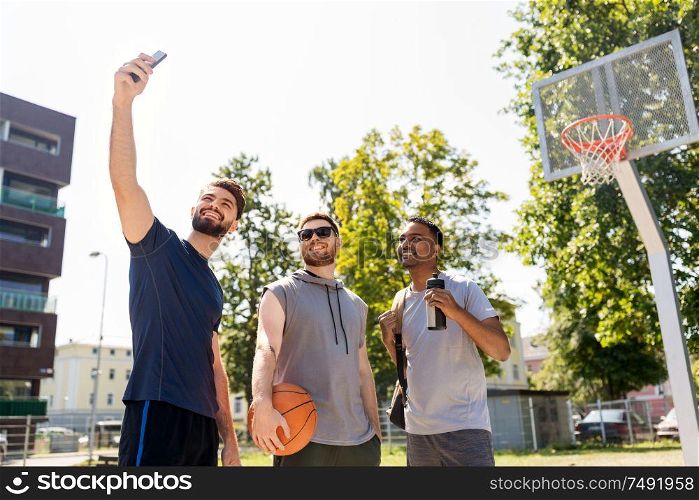sport, leisure games and male friendship concept - group of happy men or friends taking selfie by smartphone at outdoor basketball playground. happy men taking selfie at basketball playground