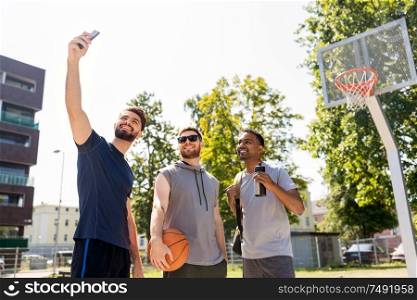 sport, leisure games and male friendship concept - group of happy men or friends taking selfie by smartphone at outdoor basketball playground. happy men taking selfie at basketball playground