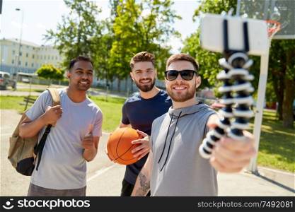 sport, leisure games and male friendship concept - group of happy men or friends taking selfie by smartphone on tripod on outdoor basketball playground. happy men taking selfie on basketball playground