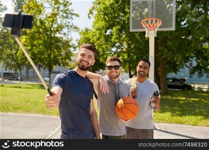 sport, leisure games and male friendship concept - group of happy men or friends taking picture by smartphone on selfie stick on outdoor basketball playground. happy men taking selfie on basketball playground
