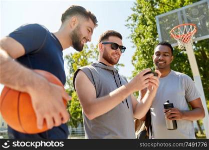 sport, leisure games and male friendship concept - group of men or friends with smartphone on outdoor basketball playground. men with smartphone on basketball playground