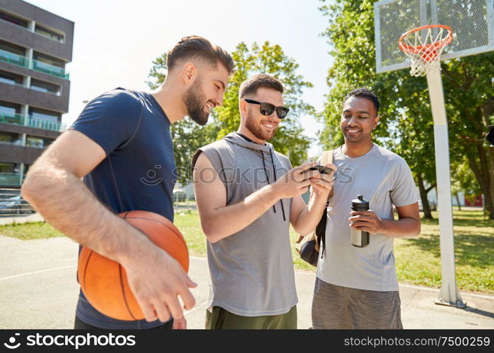 sport, leisure games and male friendship concept - group of men or friends with smartphone on outdoor basketball playground. men with smartphone on basketball playground