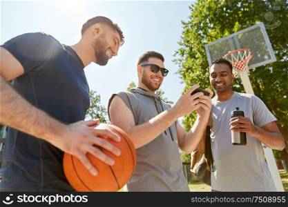 sport, leisure games and male friendship concept - group of men or friends with smartphone on outdoor basketball playground. men with smartphone on basketball playground