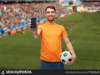 sport, leisure games and online betting concept - happy smiling man or football fan with smartphone and soccer ball over stadium background. male football fan with smartphone and soccer ball