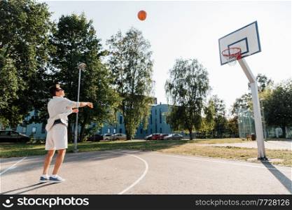sport, leisure games and people concept - young man playing basketball on outdoor playground and throwing ball to hoop. young man playing basketball on outdoor playground