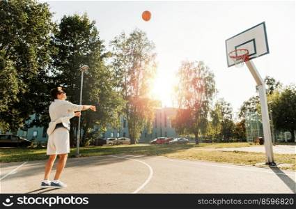 sport, leisure games and people concept - young man playing basketball on outdoor playground and throwing ball to hoop. young man playing basketball on outdoor playground